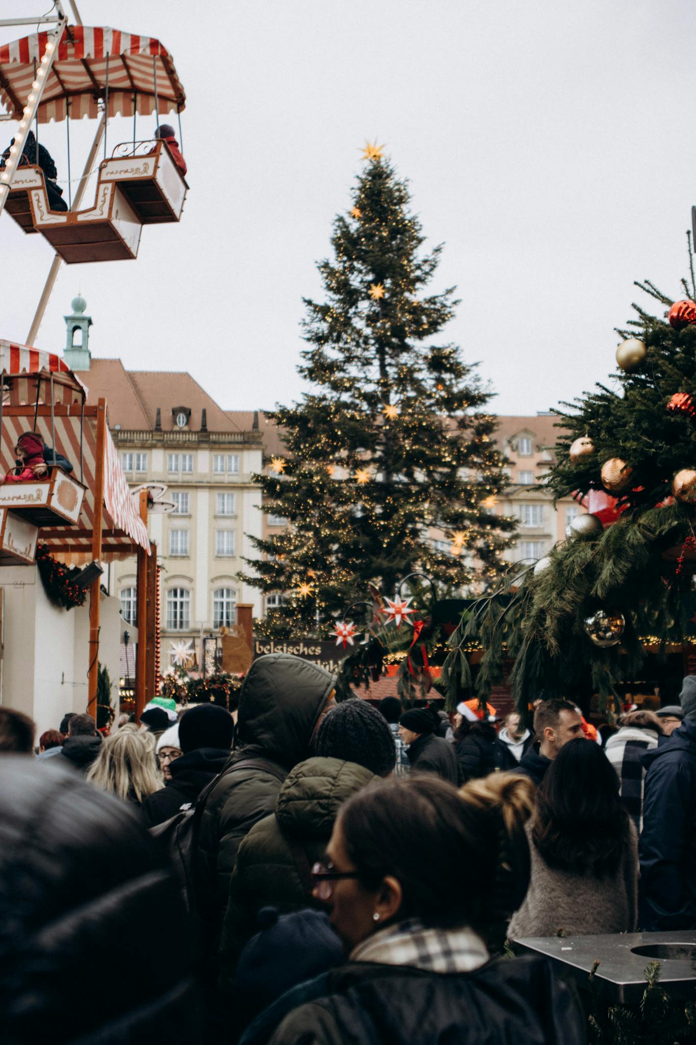 Crowded festive Christmas market featuring a large decorated tree and vibrant winter atmosphere.